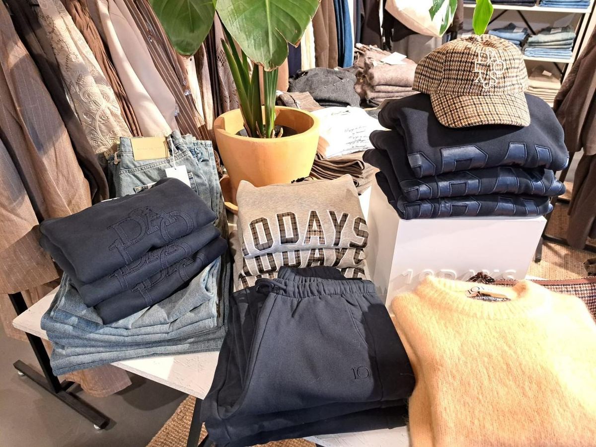 Stapels 10Days sweaters, denim en petten op een tafel